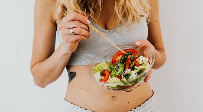 Woman in sports attire enjoys a fresh, nutritious salad, embodying a healthy lifestyle.