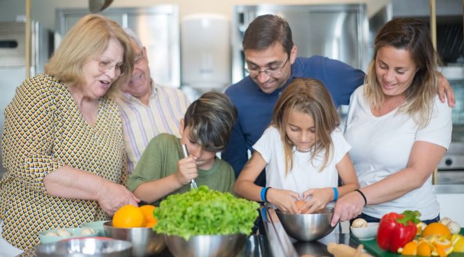 Family of various ages gathers in kitchen to cook meal together, showcasing culinary togetherness.
